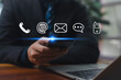 © wasan - Business communication concept with businessman using smartphone and digital contact icons representing phone, email, chat, and online connection for modern corporate communication.
