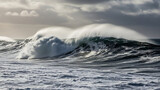A powerful ocean wave with a white spray crest crashes in the turbulent sea under a dramatic, stormy sky, showcasing the raw force of nature