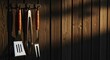 © antuanetto - Barbecue grill tools hanging on a rustic dark wooden wall with warm sunlight for outdoor cooking concept and summer gathering