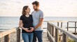 © Vasiliy - A happy pregnant couple embracing on a wooden boardwalk by the sea. Expecting parents smiling and touching the baby bump together.