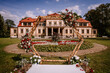 © Raivo - Elegant outdoor wedding venue featuring a beautifully landscaped garden with vibrant flowers, a decorative arch, and a historic mansion in the background, perfect for romantic ceremonies