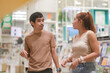 © Chocheng channel - A couple walking through a brightly lit aisle of bookshelves (likely a bookstore or mall library). The man points toward the shelves as he speaks to the woman.