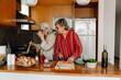 © Drobot Dean - A woman is cutting carrots and standing at the table next to her female friend who is holding a spatula in a frying pan