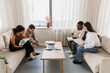 © Drobot Dean - A group of four workers hold documents and look at laptops while sitting in pairs on sofas and talking