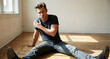 © Mariya - Concerned young man sitting on a rustic wooden floor, touching his shoulder in pain for a health issue or stress concept, illuminated by soft natural window light