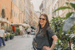 © Guillermo - Retrato estilo de vida de turista mujer sonriendo en una pintoresca calle peatonal de Roma, Italia. Arquitectura tradicional de edificios ocres y suelo de adoquines (sampietrini).