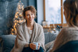 © Mike - Woman sits on couch with a drink engaged in conversation with a friend in a cozy and warm living room during winter Generative AI