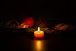 © Simplementbeau. - Petite bougie en cire naturelle orange allumée avec une flamme centrée dans l’image, ambiance de Noël, branche de sapin, ruban satin rouge et blanc, pomme, pomme de pin, petits gâteaux et anis étoilée