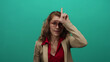 © Krakenimages.com - Woman making loser gesture with hand on forehead against isolated green wall wearing glasses and red shirt under beige jacket expressing playful attitude
