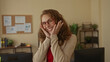 © Krakenimages.com - Woman smiling confidently in office setting, wearing glasses and blazer, surrounded by books and plants, conveying happiness and professionalism in a work environment.
