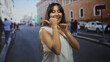 © Krakenimages.com - Young latina brunette woman smiling with thumb pointing sideways on a city street by brick building; playful confidence.