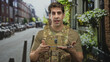 © Krakenimages.com - Man soldier in camouflage vest and dogtags holds tablet with both hands while speaking on street amid parked bikes and buildings; duty focus.