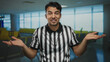 © Krakenimages.com - Young hispanic man dressed as referee gestures in an airport terminal conveying uncertainty and humor with hands up in an indoor setting.