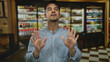 © Krakenimages.com - Young hispanic man expressing frustration with hand gestures in a casual restaurant setting, surrounded by blurred beverage shelves.