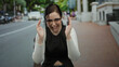 © Krakenimages.com - Brunette woman outdoors on the street makes a size gesture using her hands with expressions of surprise and focus, set against a blurred urban background.