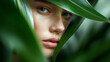 © Curioso.Photography - A close-up portrait of a woman’s face framed by lush green leaves in a natural, moody setting.