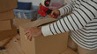 © Krakenimages.com - Man packing cardboard box in living room of new home with tape dispenser amid unpacked household items.