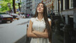© Krakenimages.com - Teenage girl with braces and long hair standing with arms crossed and smiling in a white blouse on a city street by parked cars and bollards; youthful confidence.