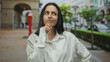 © Krakenimages.com - Woman in white shirt stands puzzled on a busy city street with her arms raised, conveying confusion and uncertainty outdoors in an urban setting.