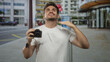 © Krakenimages.com - Man holds camera on a street beside a building while tugging his t shirt and looking up; curiosity discovery.