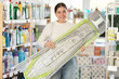 © JackF - Girl housewife in household store examines goods, chooses ironing board. Client view product, examine details of ironing board, make sure there are no defects. Buyer is shopping in household