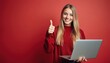 © Vadym - Young girl smiles holding laptop, gives thumbs up. She is happy and confident, showing good results on red background. Casual teen works on computer, celebrates success with gesture.