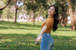© crizzystudio - Young woman smiling walking in green park inviting viewer