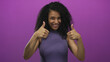 © Krakenimages.com - Young woman smiling against a vibrant purple background giving thumbs up with curly hair and wearing a sleeveless top portraying positivity and confidence