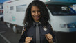 © Krakenimages.com - Young hispanic woman police officer smiling outdoors in front of police van showcasing confident law enforcement presence in city street setting.