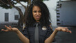 © Krakenimages.com - Young hispanic policewoman in uniform standing outdoors with questioning expression, surrounded by urban background and trees, conveying authority and command presence.