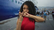 © Krakenimages.com - Woman in red dress makes hashtag gesture with fingers at port pier by a large moored ship; fun social moment.