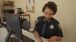 © Krakenimages.com - Policewoman in uniform working at a desk with computer and headset in a police station, taking notes, showcasing a professional environment for communication and coordination.