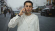© Krakenimages.com - Young man talking on smartphone in urban city street, wearing white shirt, surrounded by vehicles and buildings, illustrating communication and modern lifestyle.