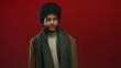 © Krakenimages.com - Man with curly hair and beard wearing scarf and jacket stands against vibrant red wall looking upwards in contemplation