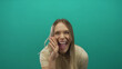 © Krakenimages.com - Young blonde woman joyfully shouting towards camera over isolated green background, highlighting expressions of excitement and enthusiasm.