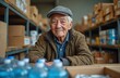 © miss irine - Elderly man in warehouse helps organize donated food and water boxes. Senior volunteer works in charity center. Generous older man assists people in need at community hub. Kindness and giving.