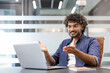 © Tetiana - Smiling young Indian man sitting at a desk and chatting on a video call, holding an online meeting