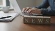© Husen - A person typing on a laptop with 'NEWS' blocks on a wooden desk, representing journalism or information.