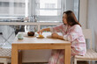 © ninelutsk - Woman having breakfast with tea and dried fruits at table by window, breakfast moment with natural daylight