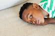 © Wavebreak Media - African American boy reclining on beige sofa cushion in living room gazing, copy space