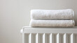© A2Z AI  - Two neatly stacked, plush white towels are placed atop a white radiator. The towels appear freshly laundered, promising a cozy, warm experience after a bath. Simple, clean style.