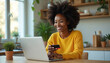 © Viktor - Smiling african american woman shops online at home using laptop computer and credit card. Happy consumer makes payment for purchases using ecommerce website. Bright interior setting.