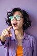 © Viktor - Young Vietnamese woman with short dark hair wears glasses and purple shirt. She points forward with open mouth and surprised wide eyes, looking upwards, against a lilac backdrop.