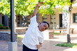 © Wavebreak Media - African boy stretching sideways at courtyard near brick planters, wearing white tee and dark shorts