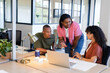 © Wavebreak Media - African American colleagues collaborating around wood desk in modern office using laptop and papers