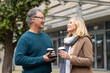© Wavebreak Media - Senior couple holding coffee cups and using smartphone standing on plaza outside modern building