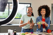 © Wavebreak Media - Diverse female friends chopping vegetables under ring light in kitchen, holding avocado, cucumbers