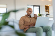 © Wavebreak Media - African American man holding coffee mug while typing on silver laptop on sofa in living room