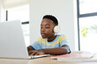 © Wavebreak Media - African American school-age boy sitting at desk with headphones studying on laptop in study corner
