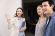 © fizkes - Cheerful realtor holding tablet, gestures invitingly while showing to young couple modern home, explain facilities, benefits location standing together on house porch. Real estate purchase, renting